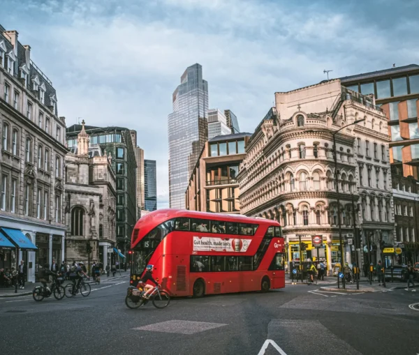 A red double decker bus drives through a busy city intersection, surrounded by historic and modern buildings—a classic urban scene, much like the uk competition watchdog navigating antitrust actions against tech giants such as apple.