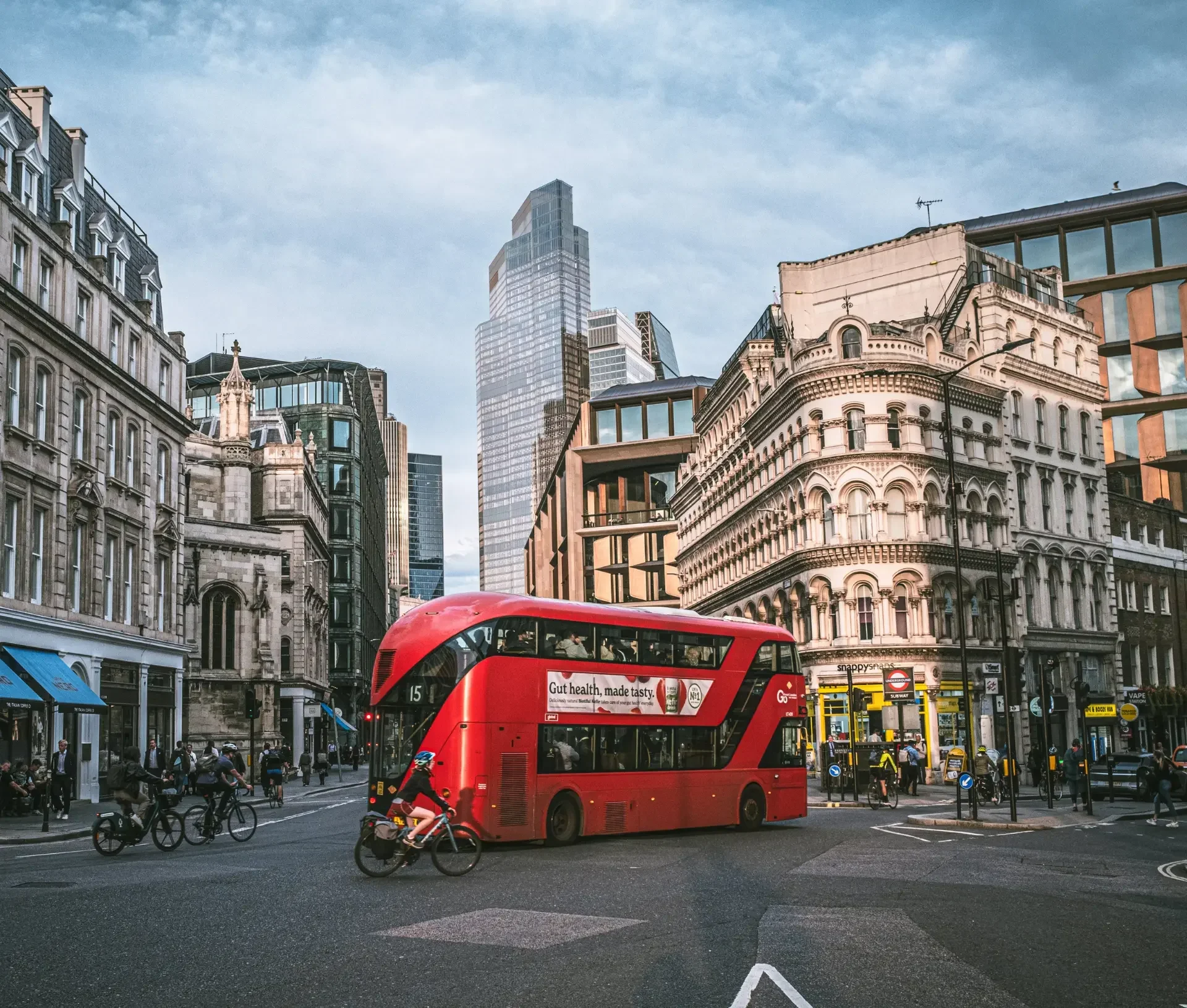 A red double decker bus drives through a busy city intersection, surrounded by historic and modern buildings—a classic urban scene, much like the uk competition watchdog navigating antitrust actions against tech giants such as apple.