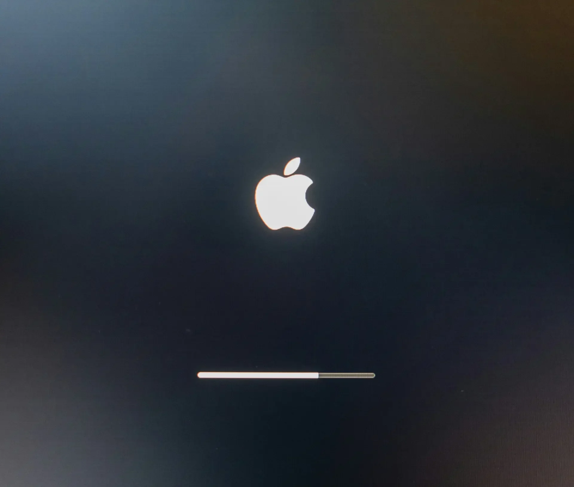 A mac computer screen displays the iconic apple logo above a loading=