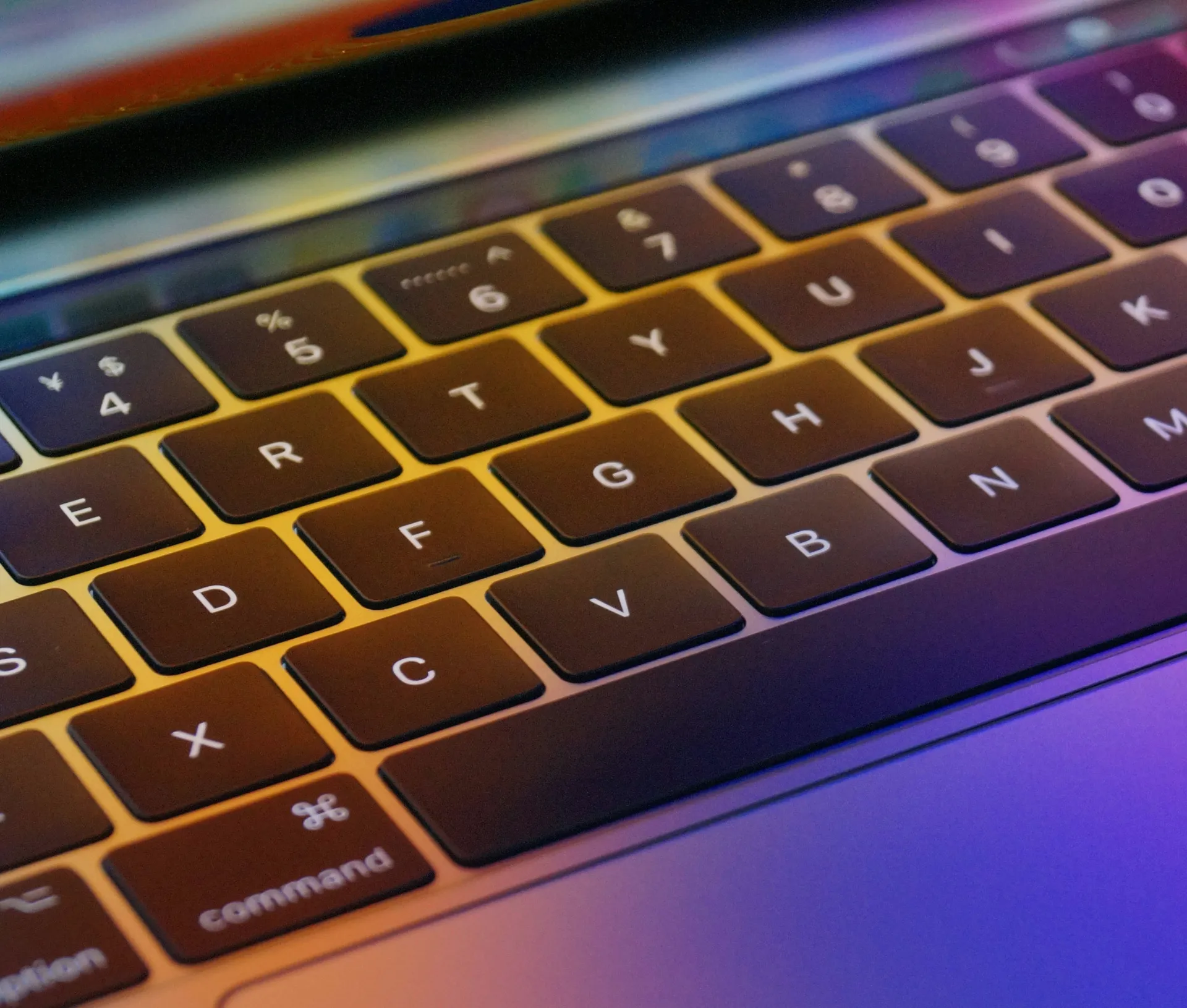 Close up of a laptop keyboard with colourful light reflections on the keys, showing details of letters, symbols, and Apple shortcuts—perfect for visualising automation in agency tasks.