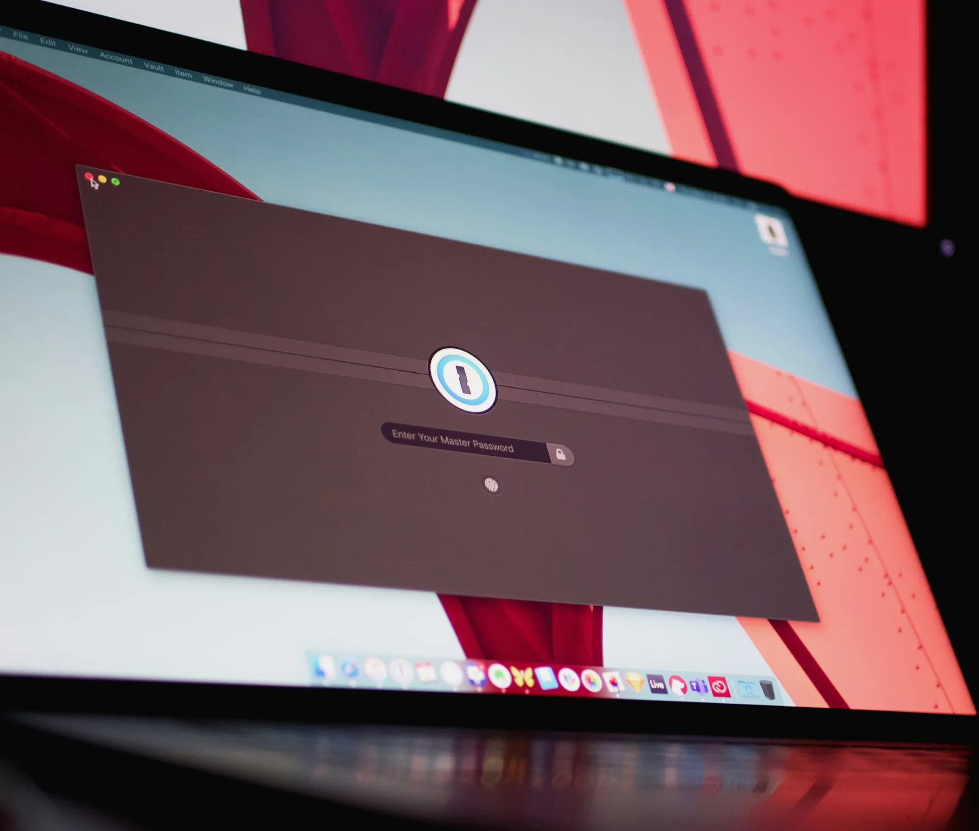 A computer screen displays the 1Password login window, prompting the user to enter their master password—showcasing the importance of a reliable password manager for team security. The desktop background shows abstract red and white shapes, with app icons visible at the bottom.