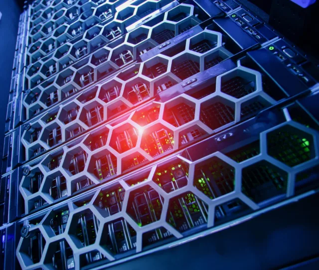 Close up of server racks with a honeycomb grille pattern, illuminated by blue and red lights, showing computer hardware and internal components in a data centre designed for advanced vulnerability detection and CVE detection.