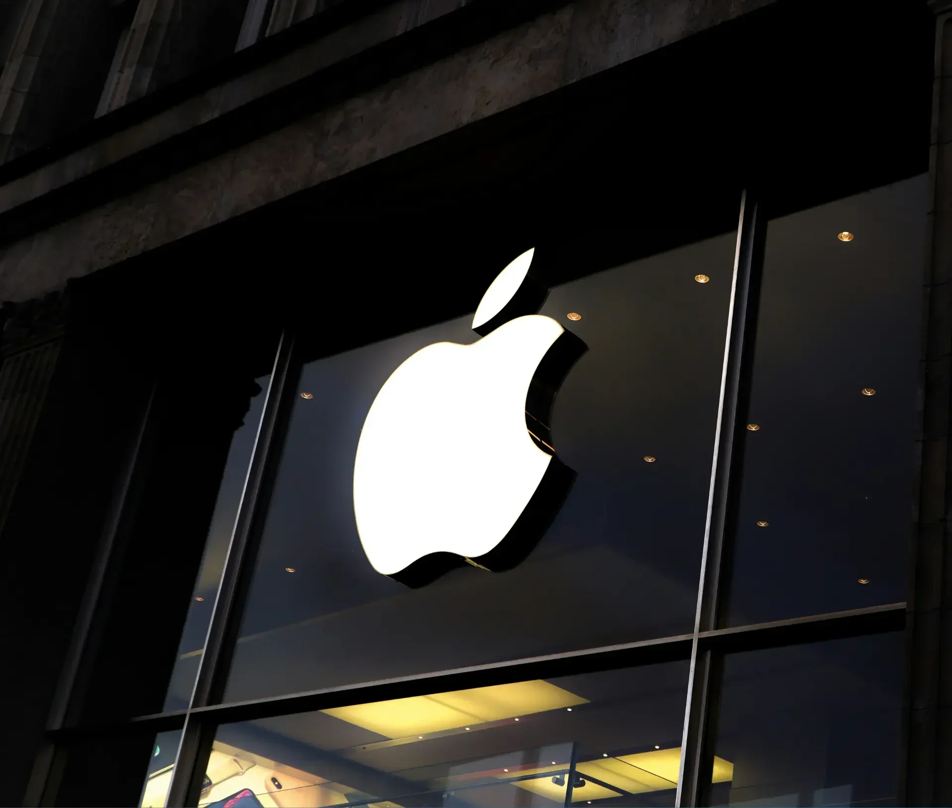 Large white apple logo illuminated on the exterior glass wall of an apple store, viewed from a low angle at dusk—a symbol of innovation and commitment to encryption and user privacy.
