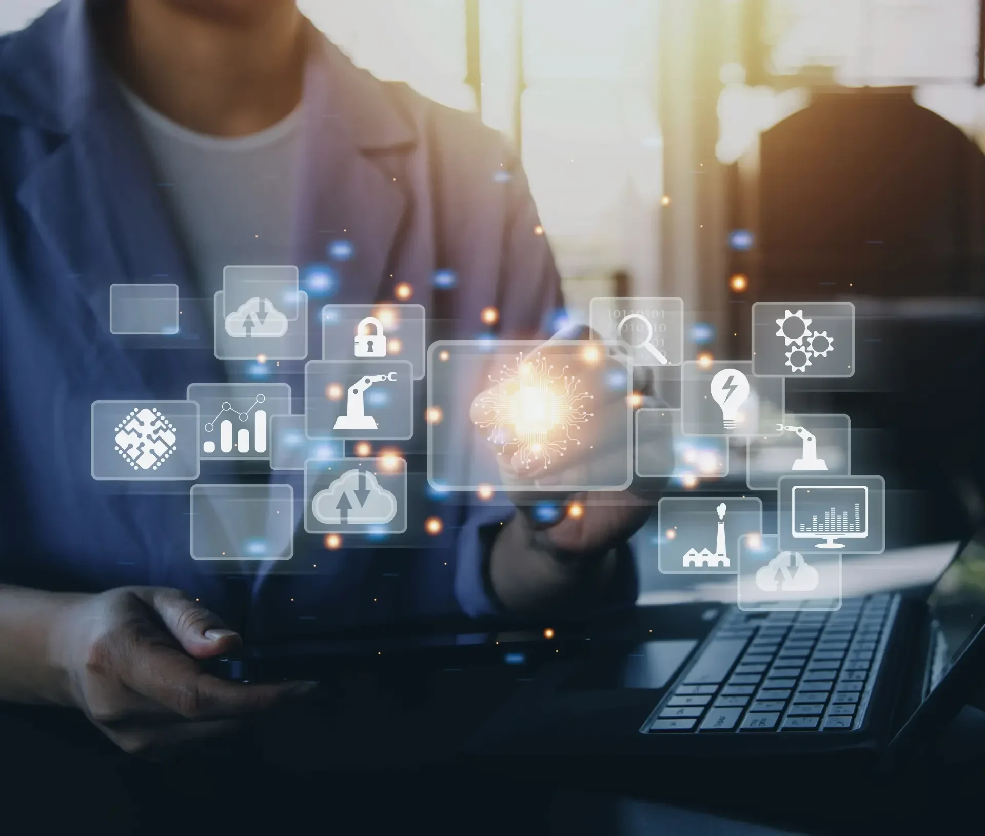 Person using a laptop and tablet with floating digital icons representing ai adoption, technology, automation, and industrial processes as part of a modern it strategy in a contemporary workspace.