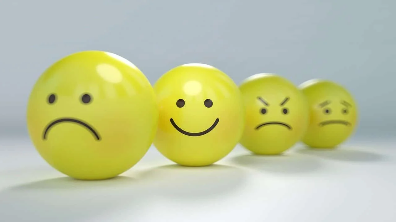 Four yellow spheres with drawn faces showing emotions—sad, happy, angry, and confused—are arranged in a line, perfectly capturing how teams might feel during a change it provider transition.