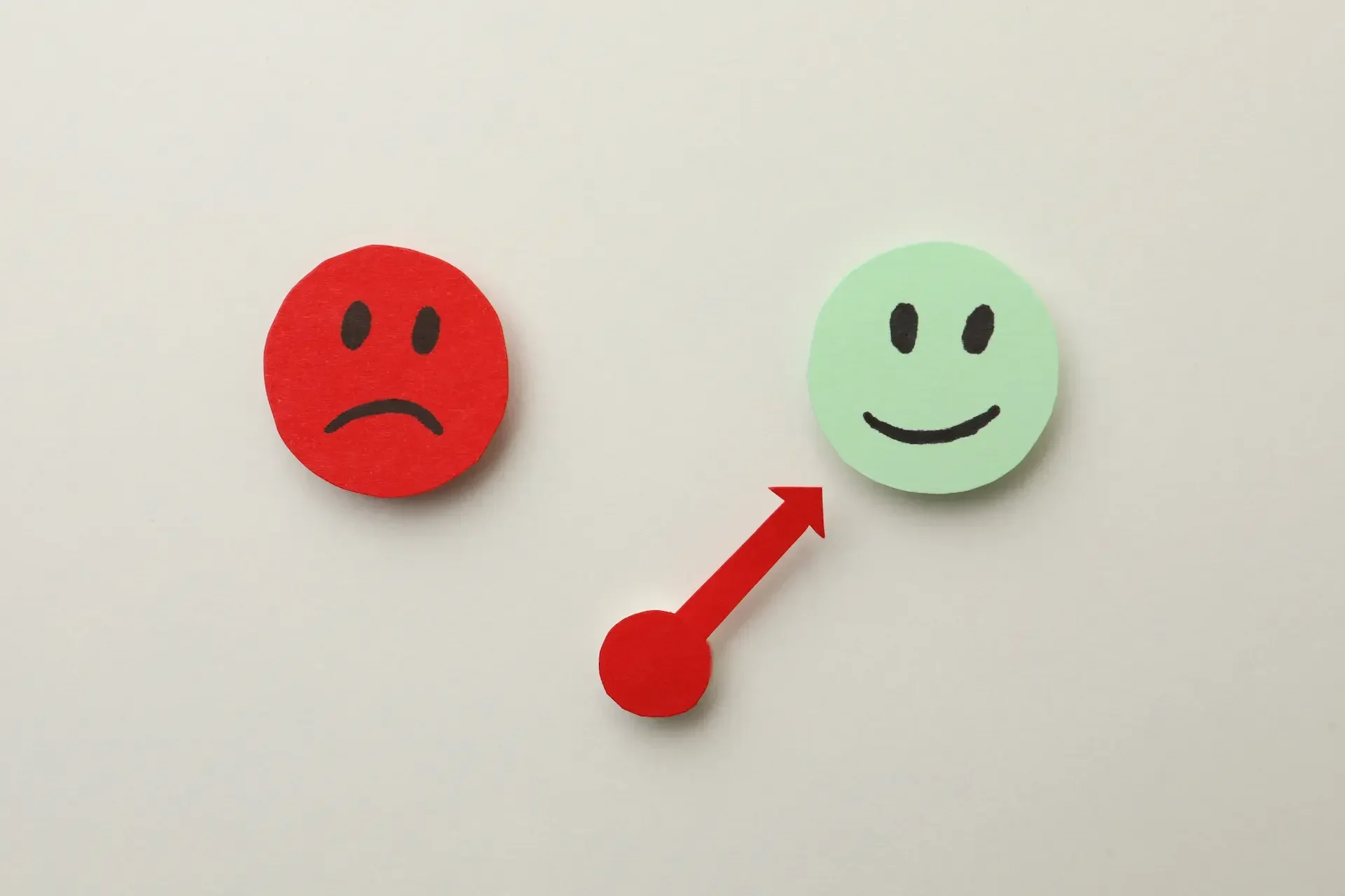 A red sad face transitions to a green happy face, connected by a red arrow pointing from left to right—illustrating how tech teams can improve mental health by working smarter.
