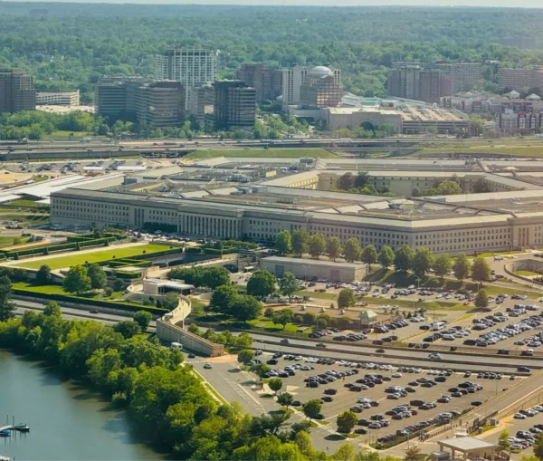 Aerial view of the Pentagon, as if processed by AI removal, surrounded by car parks, motorways, and the Arlington skyline.
