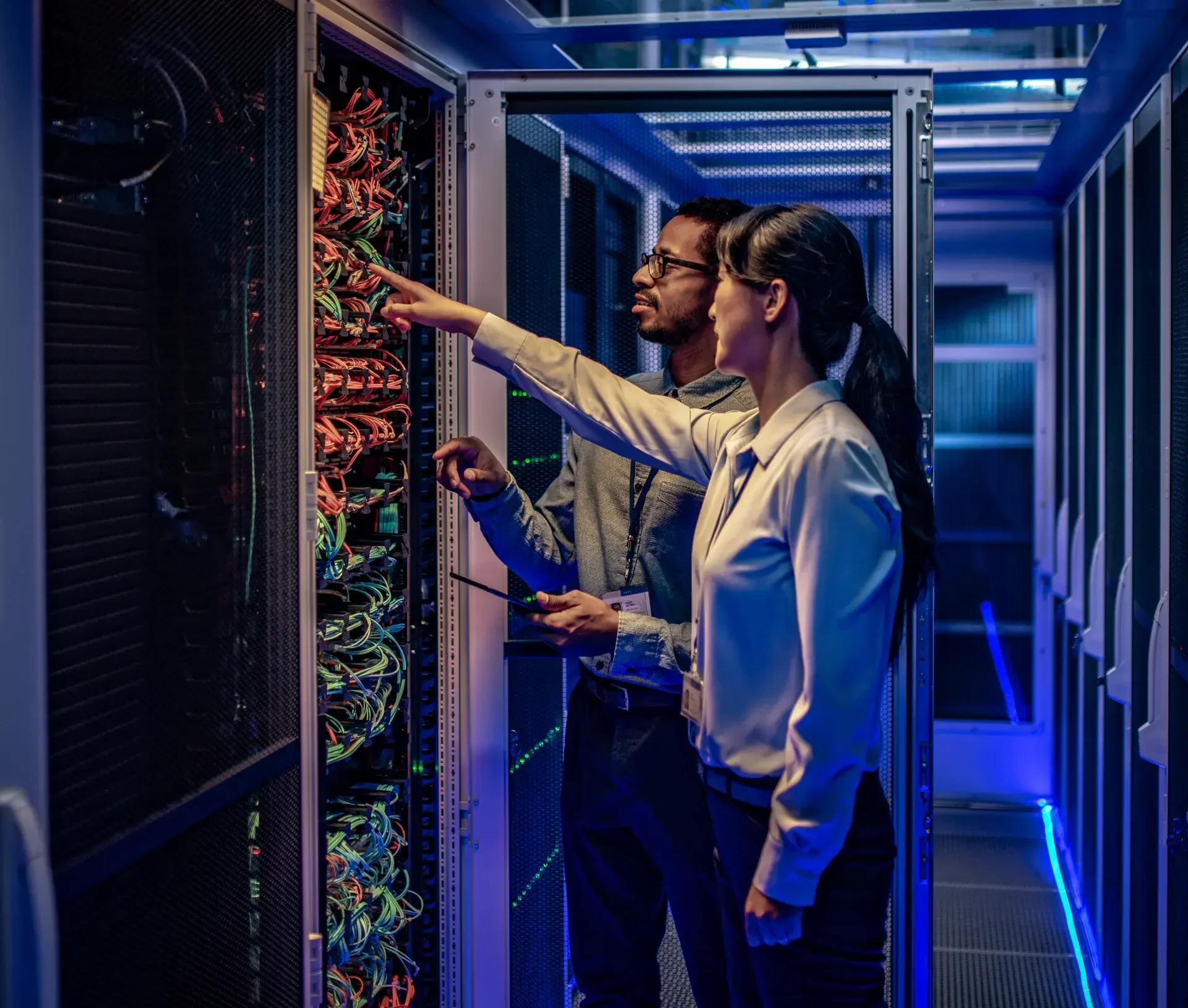 Two professionals examine and point at cables and hardware inside a server rack in a data center, ensuring top notch it support and proactive it monitoring for seamless operations.