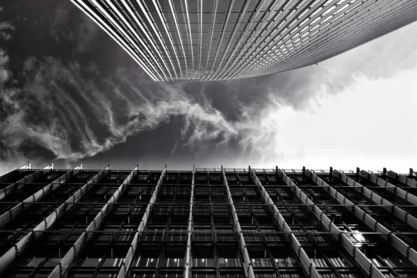 A black and white photo of two tall buildings taken from a low angle, with dramatic clouds in the sky above—capturing the ambition of scaling firms reaching new heights.