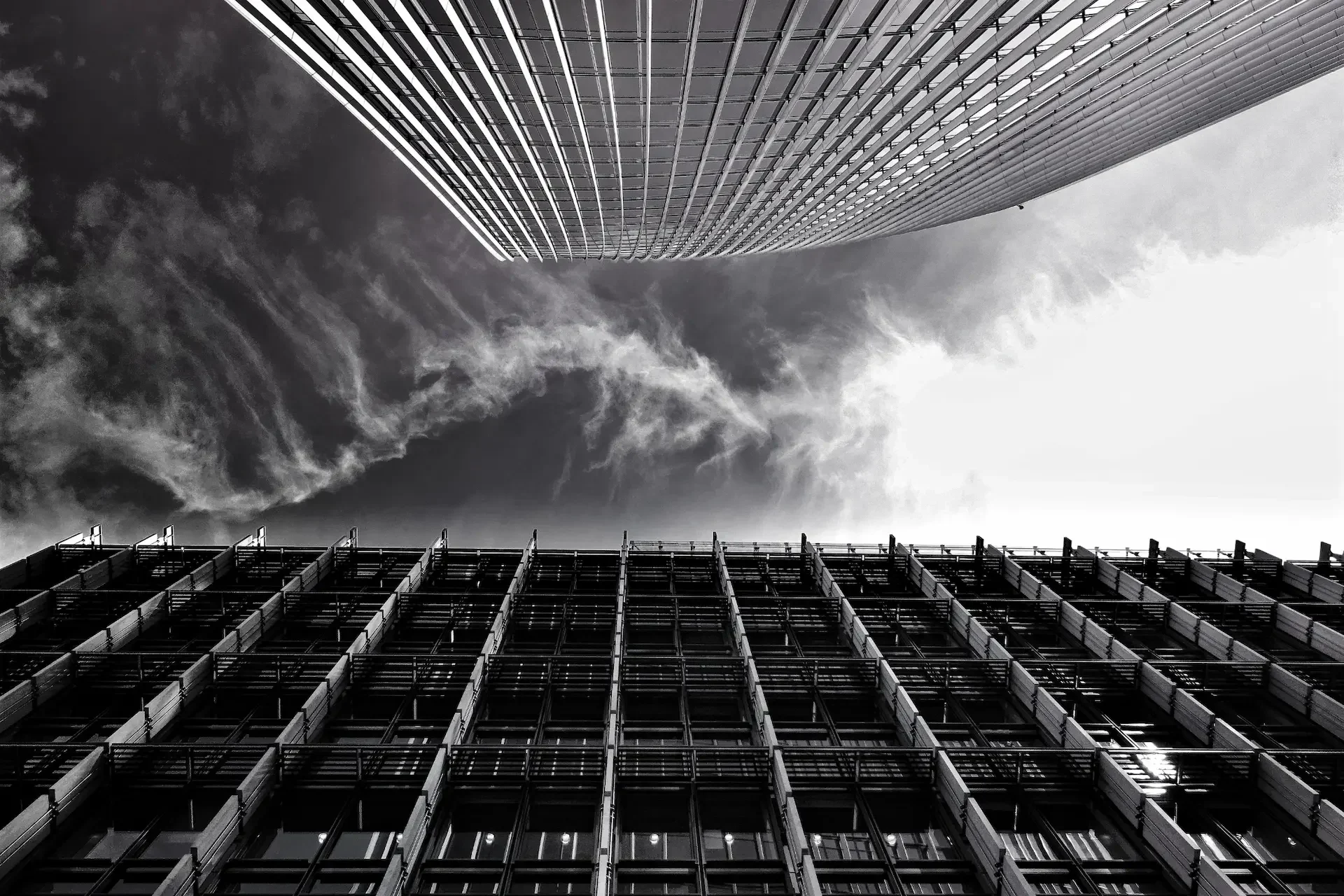 A black and white photo of two tall buildings taken from a low angle, with dramatic clouds in the sky above—capturing the ambition of scaling firms reaching new heights.