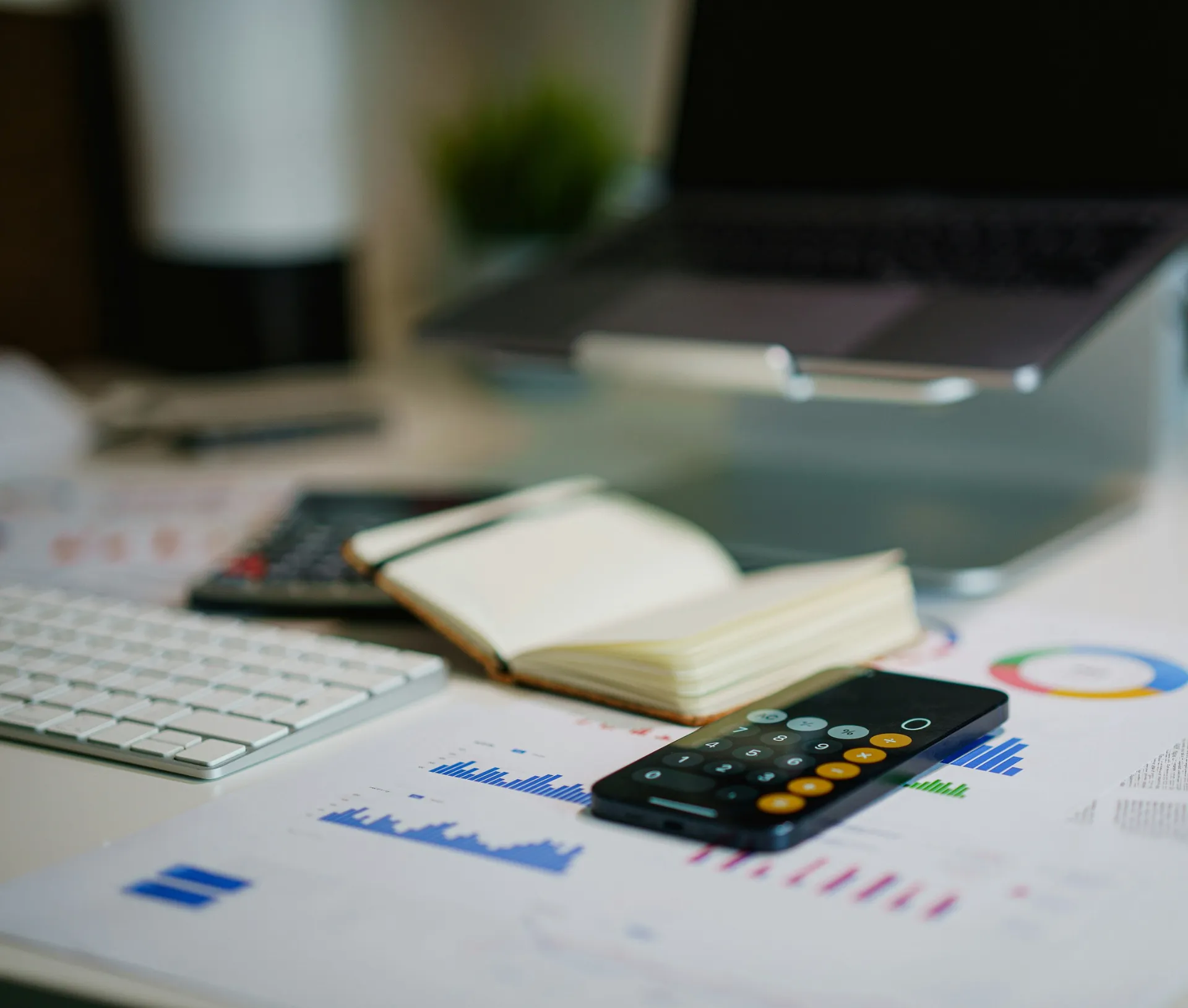 A workspace with a laptop, keyboard, open notebook, calculator, and printed charts with graphs and data—alongside QuickBooks open on the screen—suggests financial or business analysis with an emphasis on maintaining a clear audit trail.