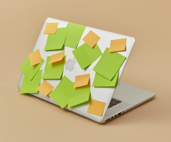 A laptop with its top panel covered in vibrant green and yellow sticky notes, isolated on a beige background.