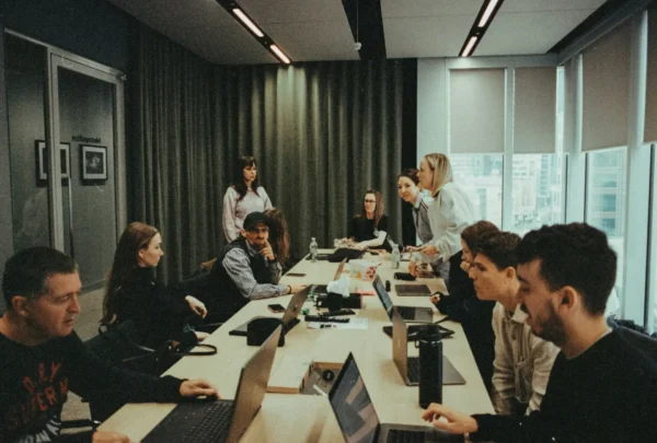 A group of people sit around a conference table with laptops and papers, discussing it as a service (itaas) as more companies make the switch in a modern office setting.
