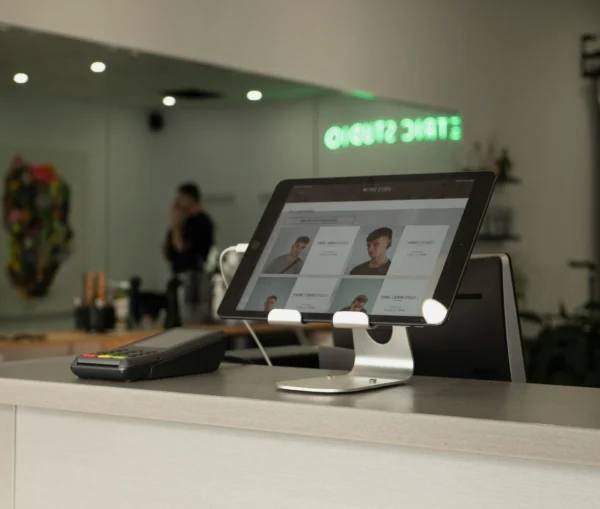 A tablet screen displaying a salon booking interface on a reception counter, with a payment terminal nearby.