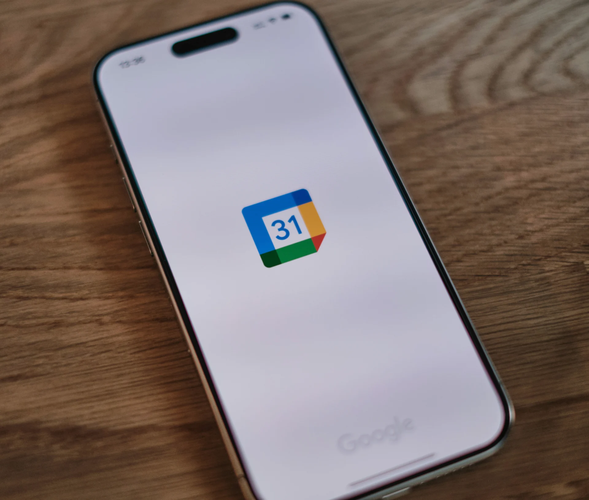 A smartphone screen displaying the Google Calendar app icon on a wooden surface.