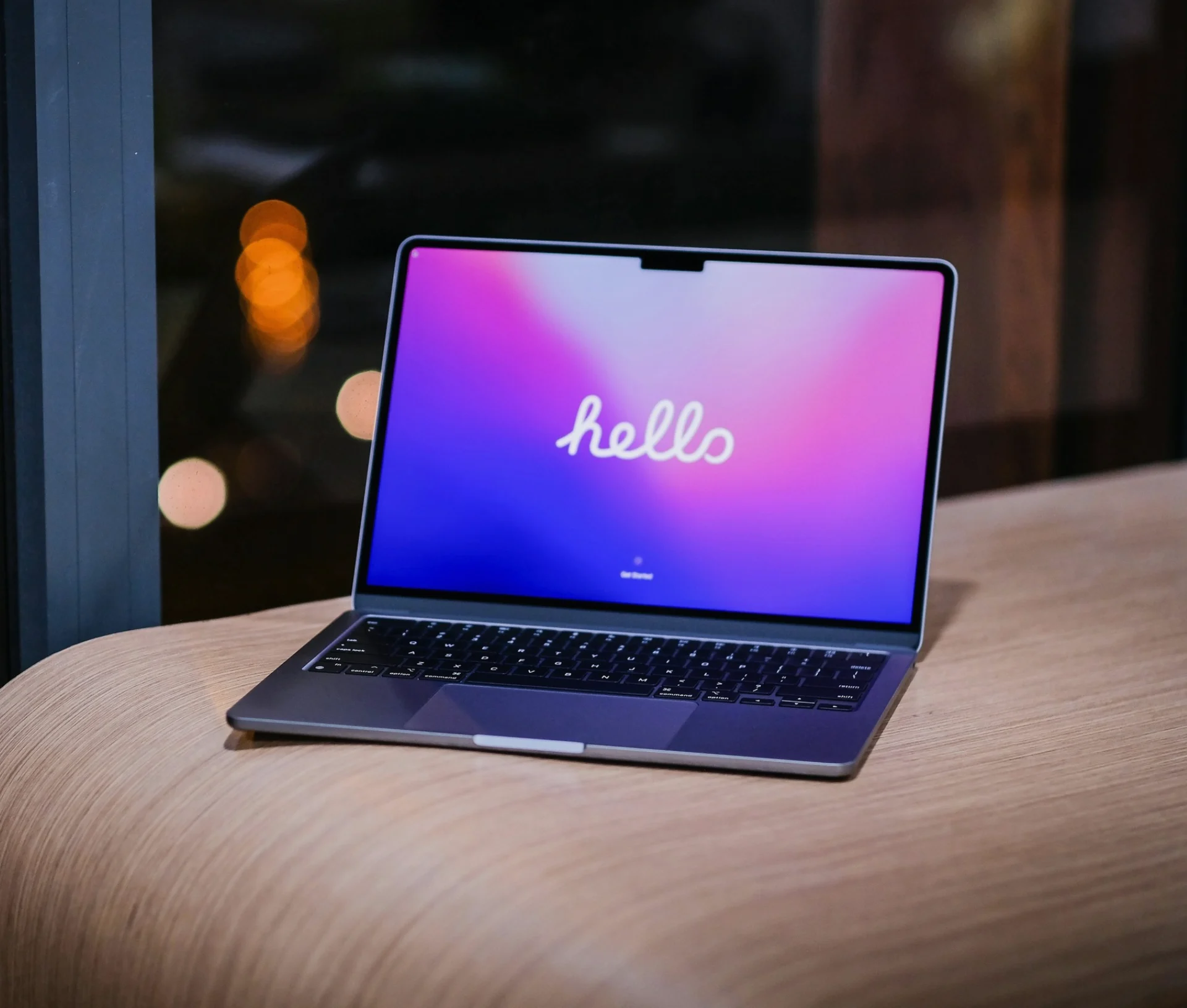 A laptop sits on a wooden surface displaying “hello” in cursive on a colourful gradient screen as the user prepares the Mac for sale.