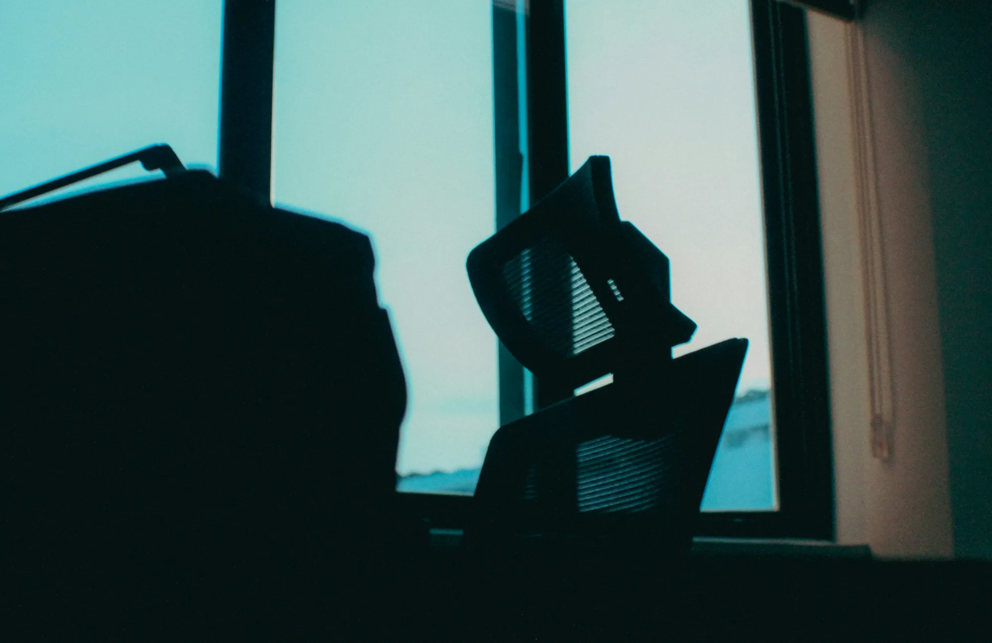 A dark silhouette of an empty office chair is in front of a large window with blue and pink light coming through at dusk or dawn, evoking a quiet moment of reflection perhaps after intense regulatory co ordination within a tight 72 hour window.