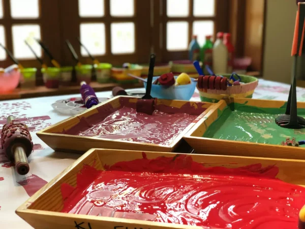 Three wooden trays filled with red, pink, and green paint are set on a table, with various painting tools and bottles in the background—much like an artist's setup for illustrating the impact of a high profile data breach.
