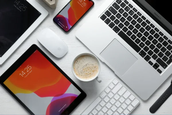 Laptop, smartphone, tablet, mouse, keyboard, and a cup of coffee arranged on a white desk—perfect for staying organized with google drive.
