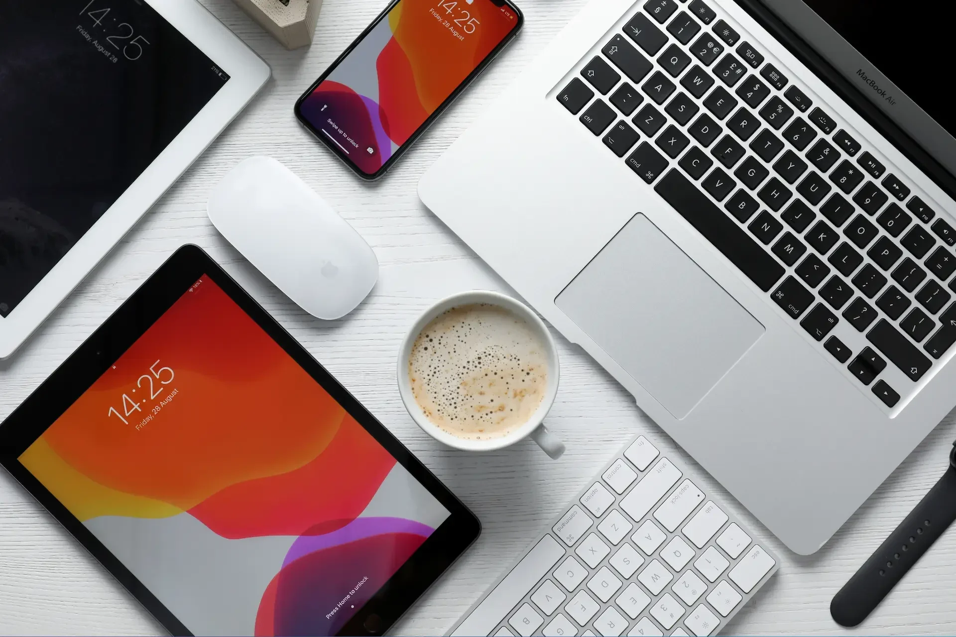 Laptop, smartphone, tablet, mouse, keyboard, and a cup of coffee arranged on a white desk—perfect for staying organized with google drive.