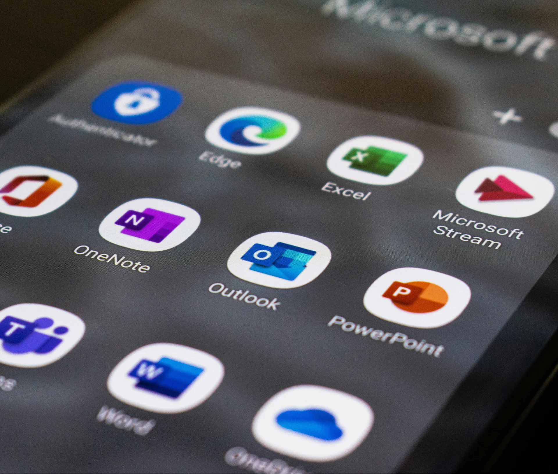 A smartphone screen displaying a grid of Microsoft 365 app icons, including Edge, Excel, OneNote, Outlook, PowerPoint, and Word.