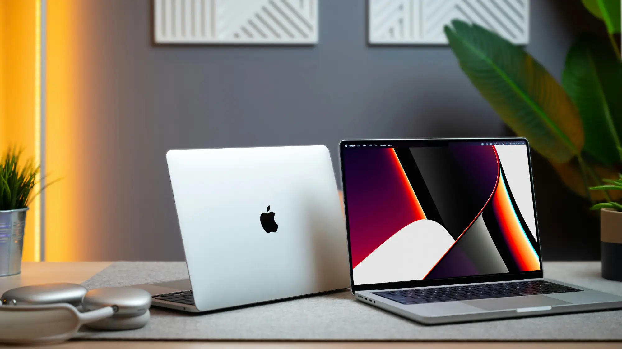 Two Apple MacBook laptops sit on a desk; one is open displaying a colourful screen related to data privacy, and the other is closed showing the Apple logo. Headphones, a plant, and decor are also visible in this modern workspace setting.
