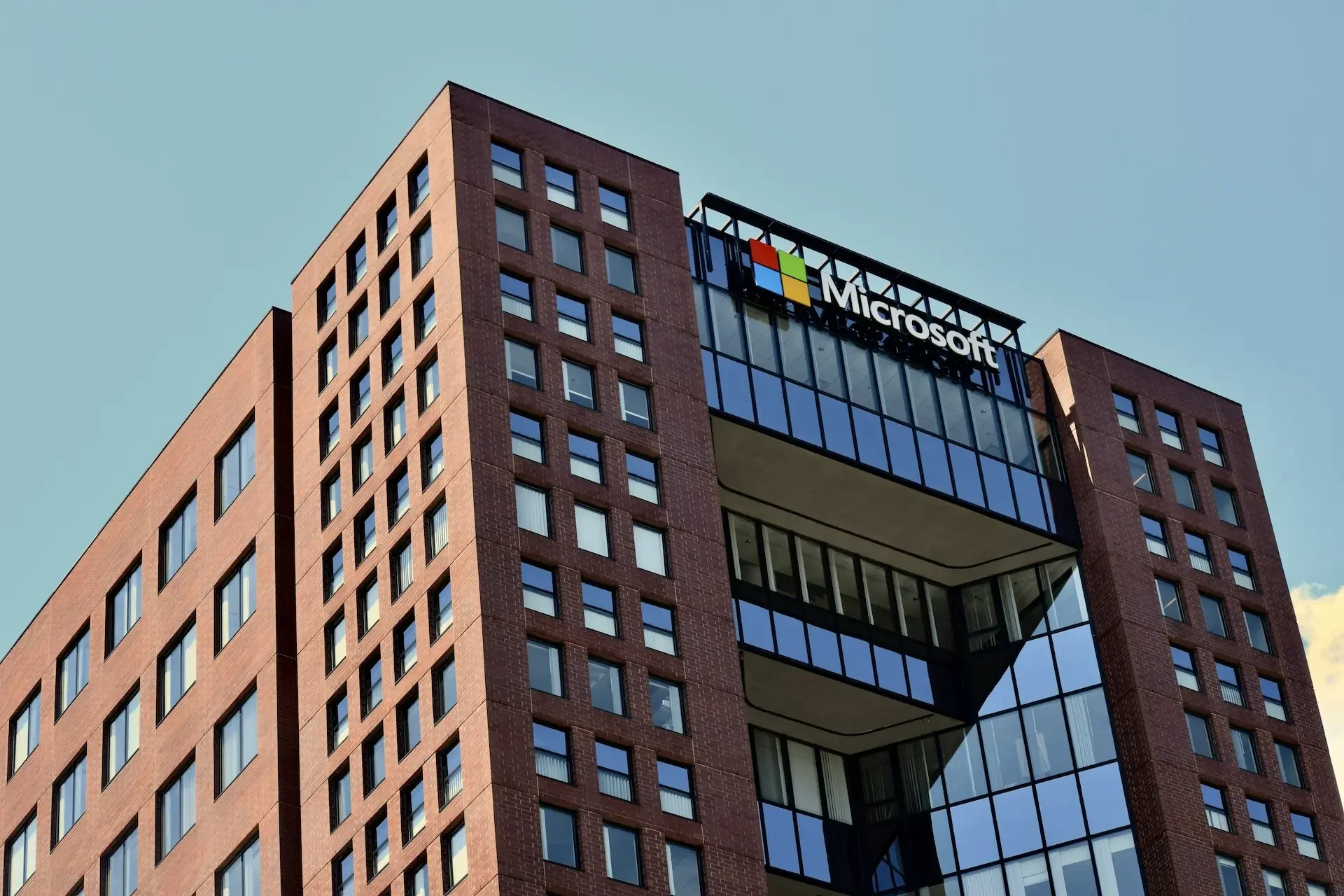 A modern office building with a red brick facade and large glass windows, featuring the microsoft logo near the top against a clear sky, showcases innovative spaces where generative ai empowers collaboration for companies like accenture.