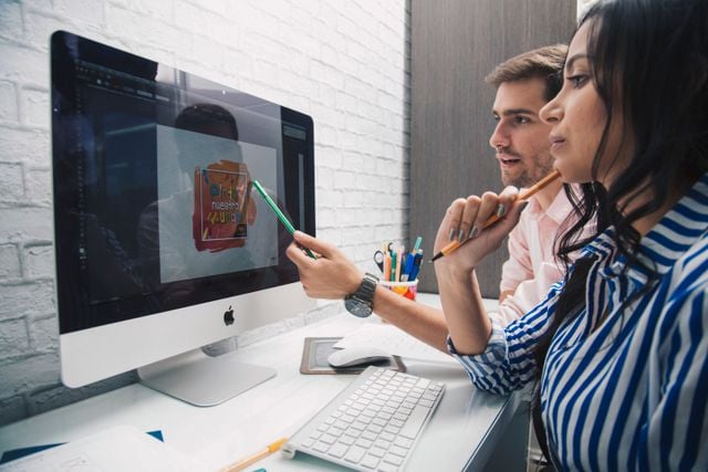 Side view of focused coworkers working together on graphic design while sitting at table and looking at monitor in modern office