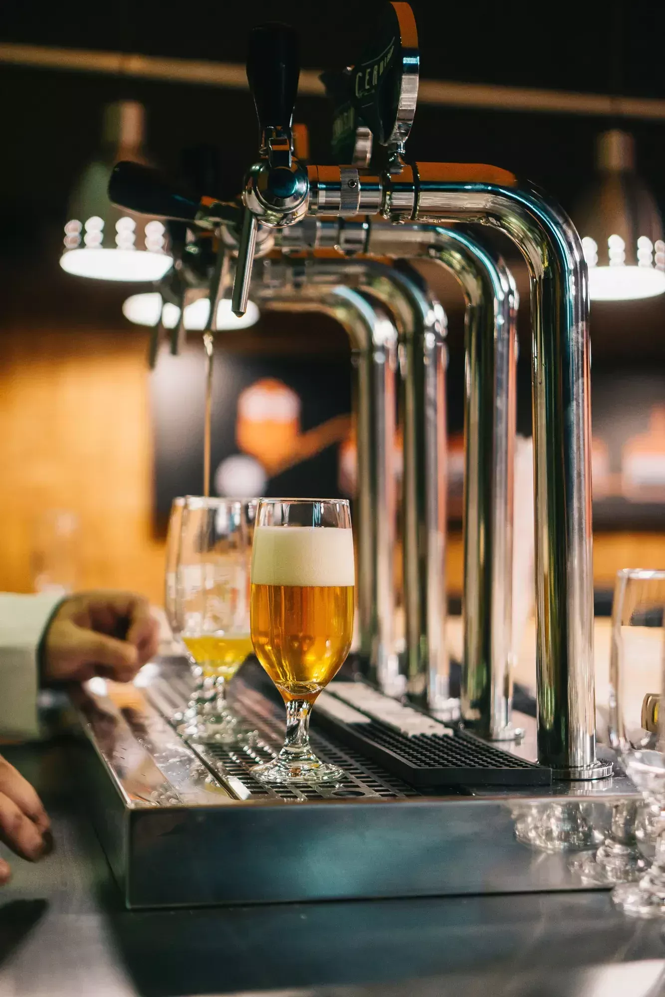 A close-up of a Camden Town Brewery setup reveals beer taps with two partially filled glasses on a shiny metal surface, enhanced by ambient lighting.