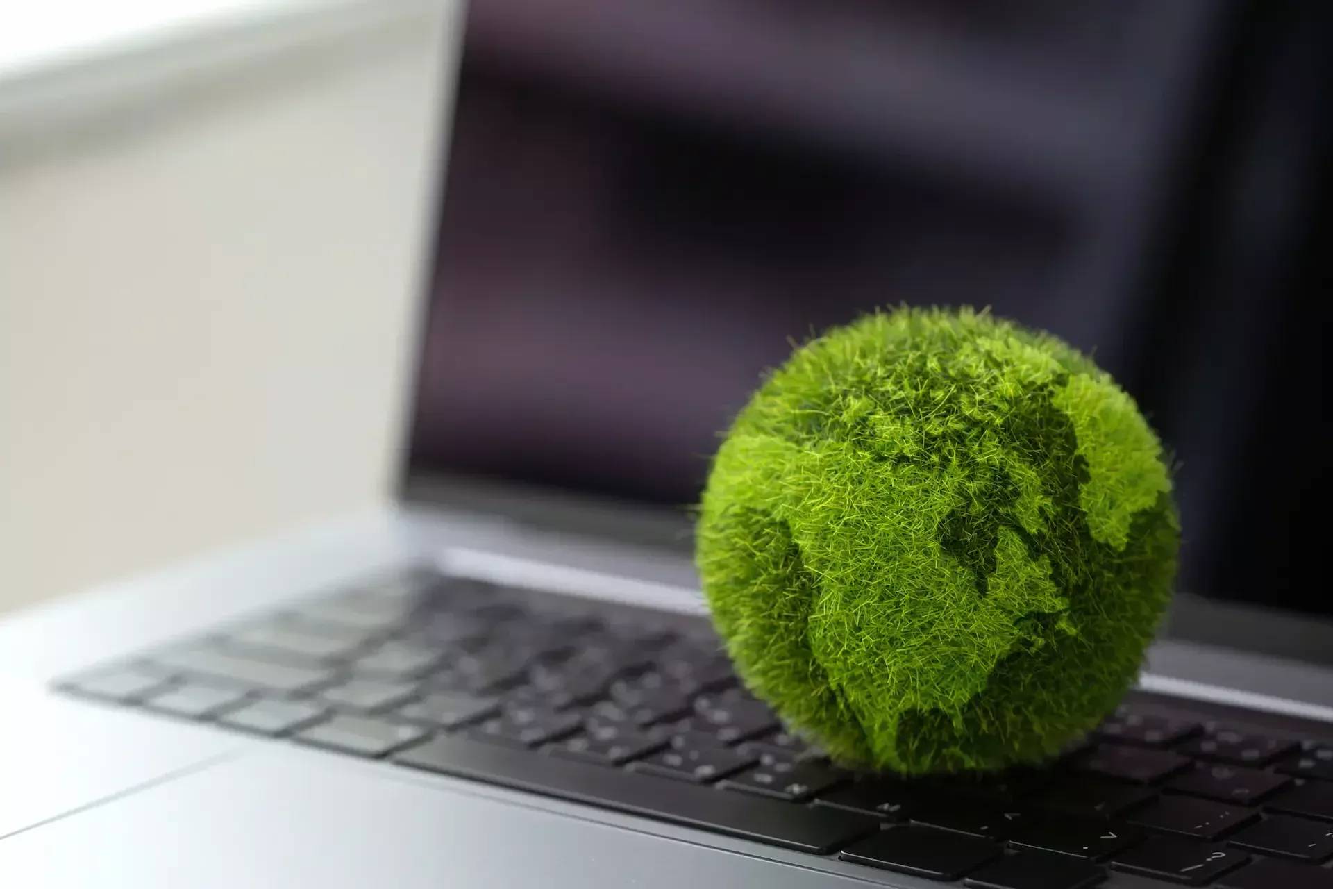 A small green globe covered in grass like texture sits on the keyboard of an open laptop, symbolizing smarter choices for a greener planet through it greener solutions.