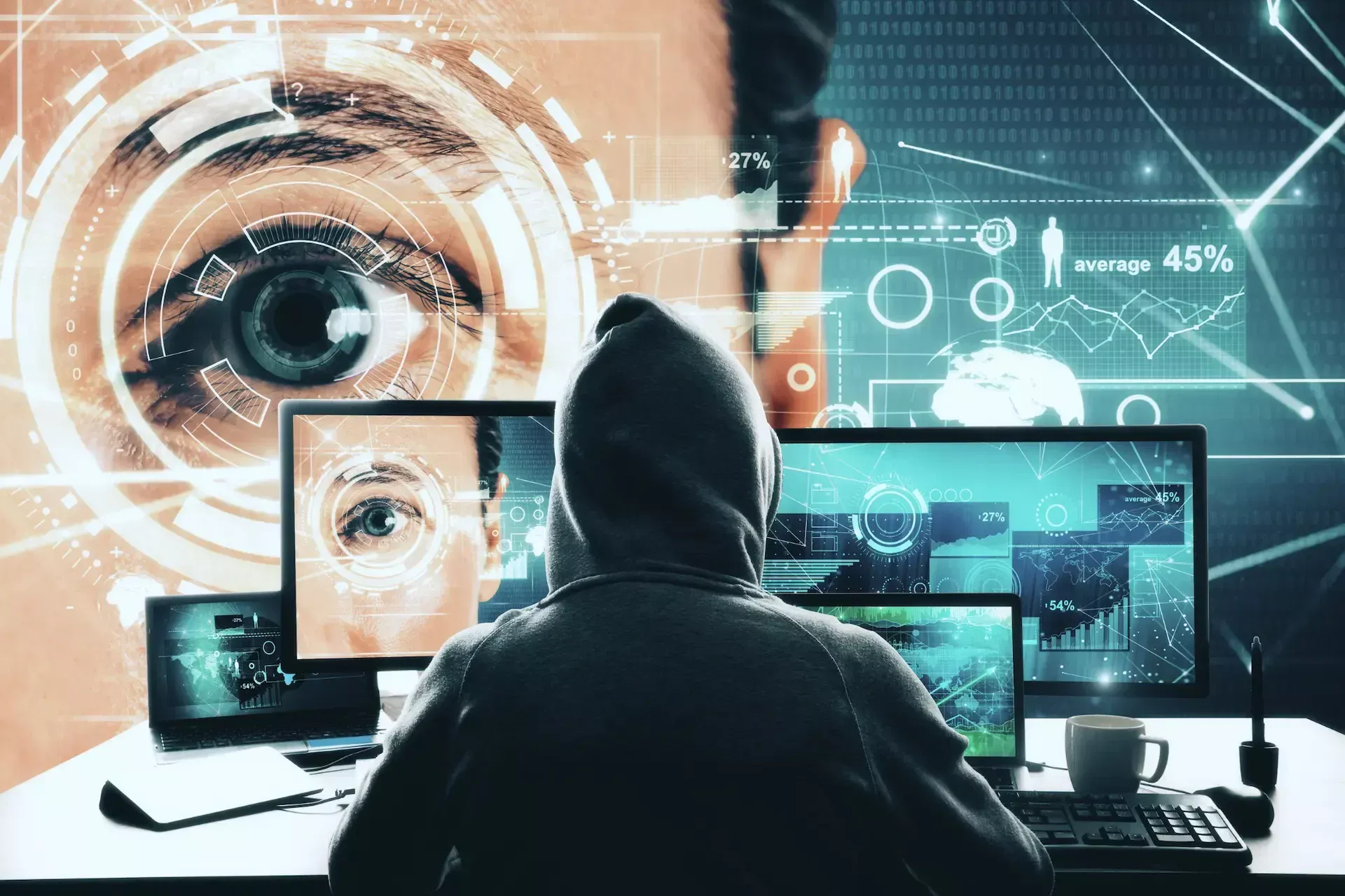 A person in a hoodie sits at a desk with multiple computer screens displaying digital graphics of eyes and data, highlighting business security risks and the monitoring of public team information against cyber threats.