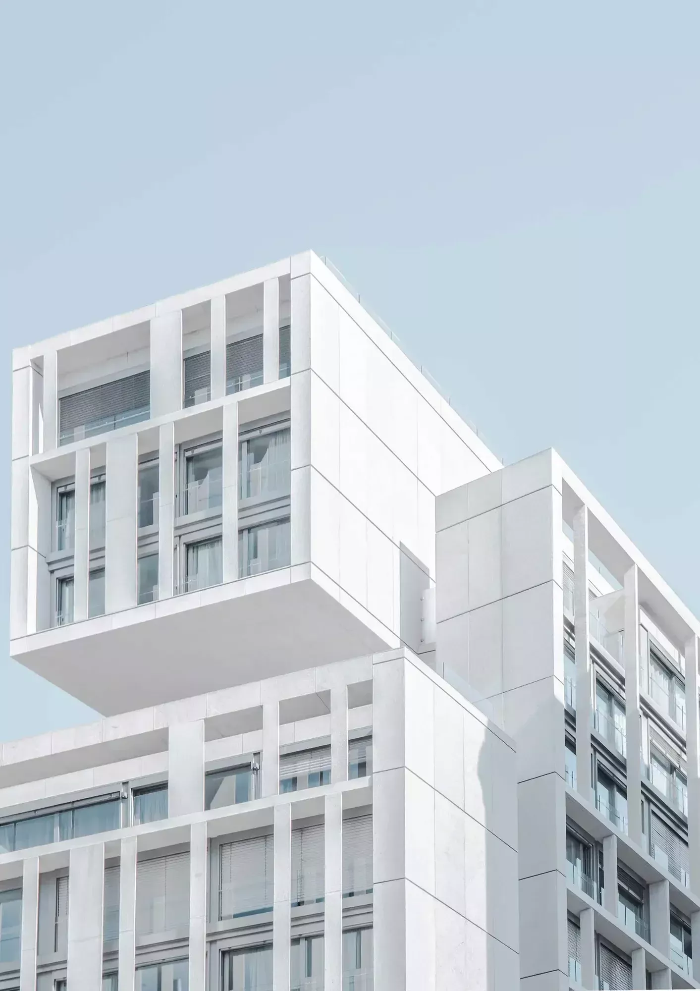The modern white building, designed by Bisset Adams, showcases a striking geometric design with large windows and a cantilevered upper section against the clear blue sky.